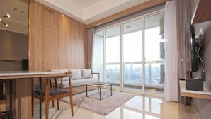 Een moderne woonkamer met een bank, een salontafel, een televisie en een balkon met uitzicht op de stad.