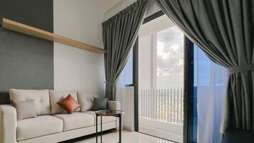 A modern living room with a sofa, a small table, and large windows with curtains.