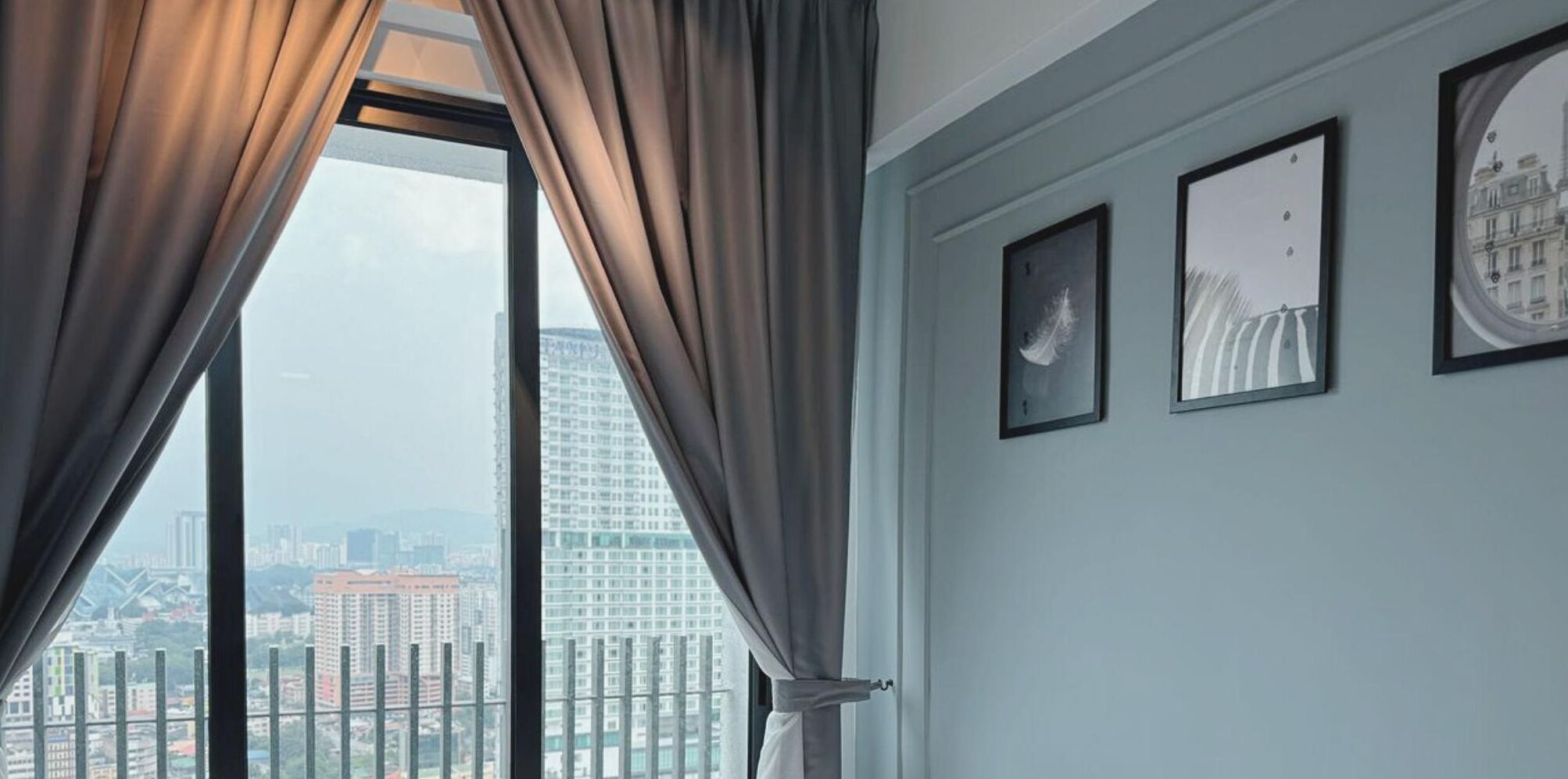 A room with a large window, curtains, and three framed pictures on the wall.