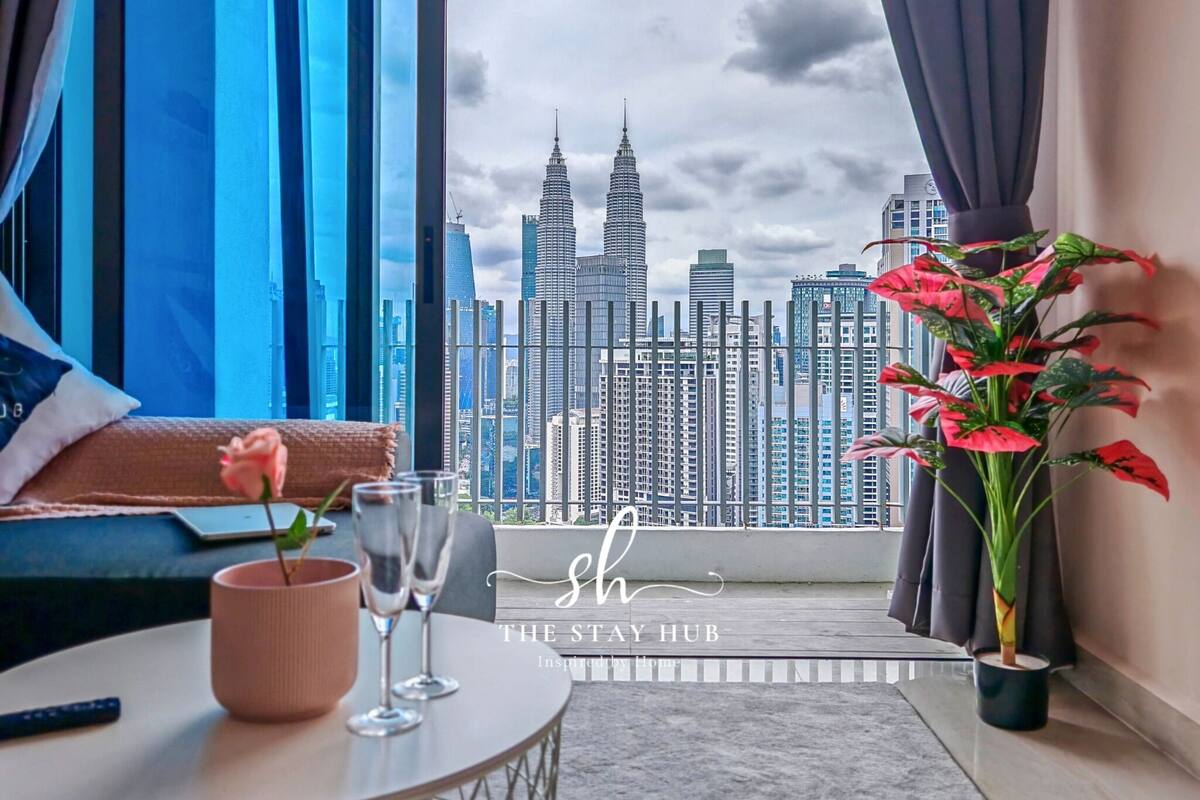 A modern room with a large window overlooking a cityscape, featuring high-rise buildings and a view of the Petronas Towers.