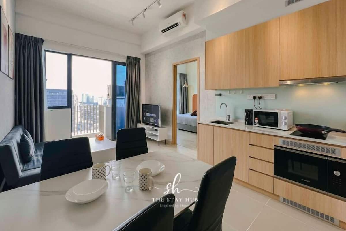 A modern apartment with a dining area, kitchen, and a large window offering a city view.