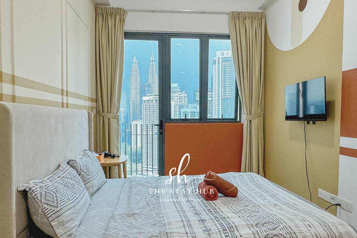 A hotel room with a large bed, a TV mounted on the wall, and a view of tall buildings through the window.