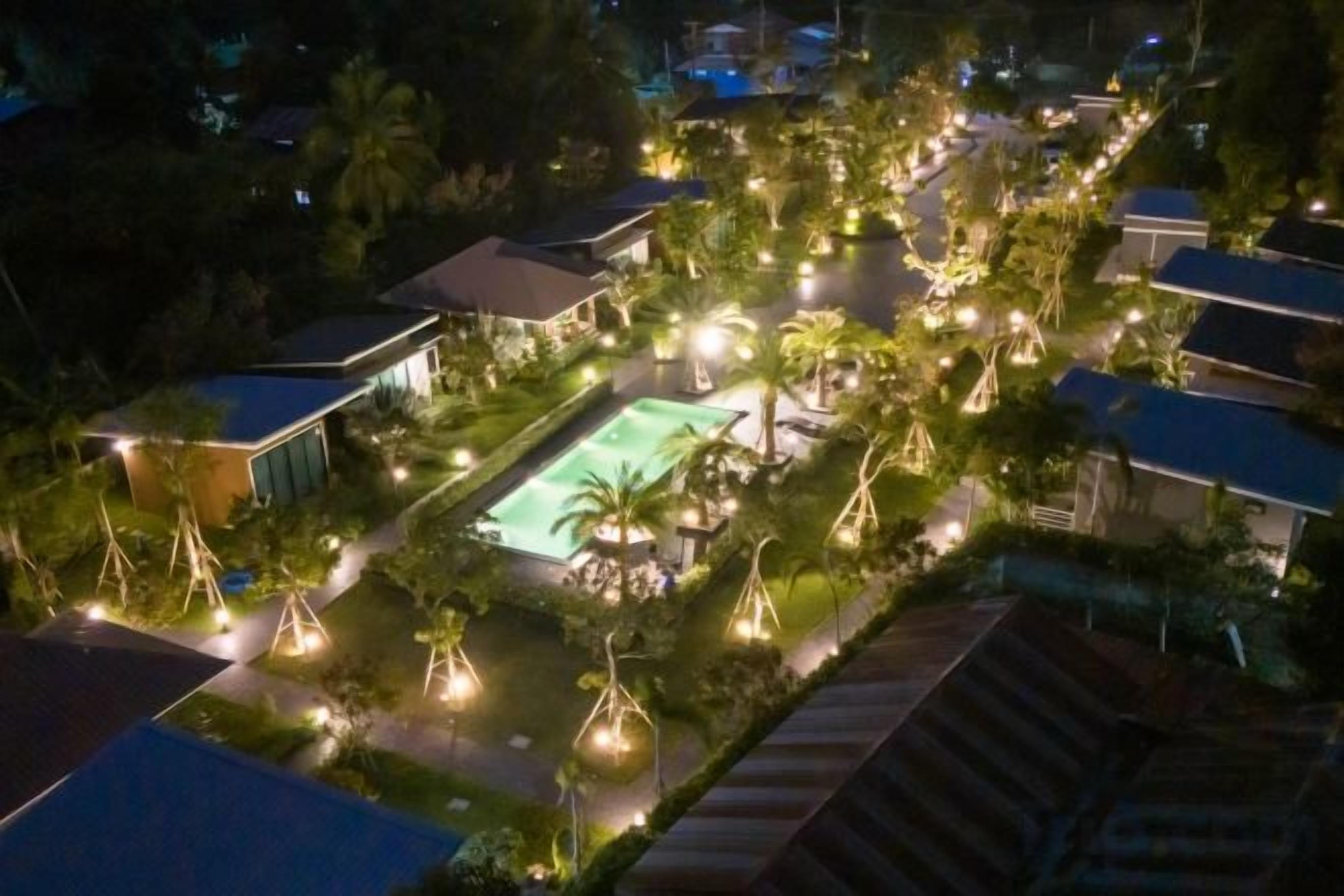 Een luchtbeeld van een resort met een zwembad, omringd door palmbomen en verlicht met lichtslingers.