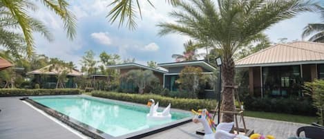 A swimming pool with swan and unicorn inflatable toys, surrounded by palm trees and modern buildings.