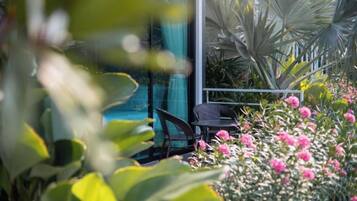 Un área de patio con una mesa y sillas, rodeada de abundante follaje y plantas con flores.