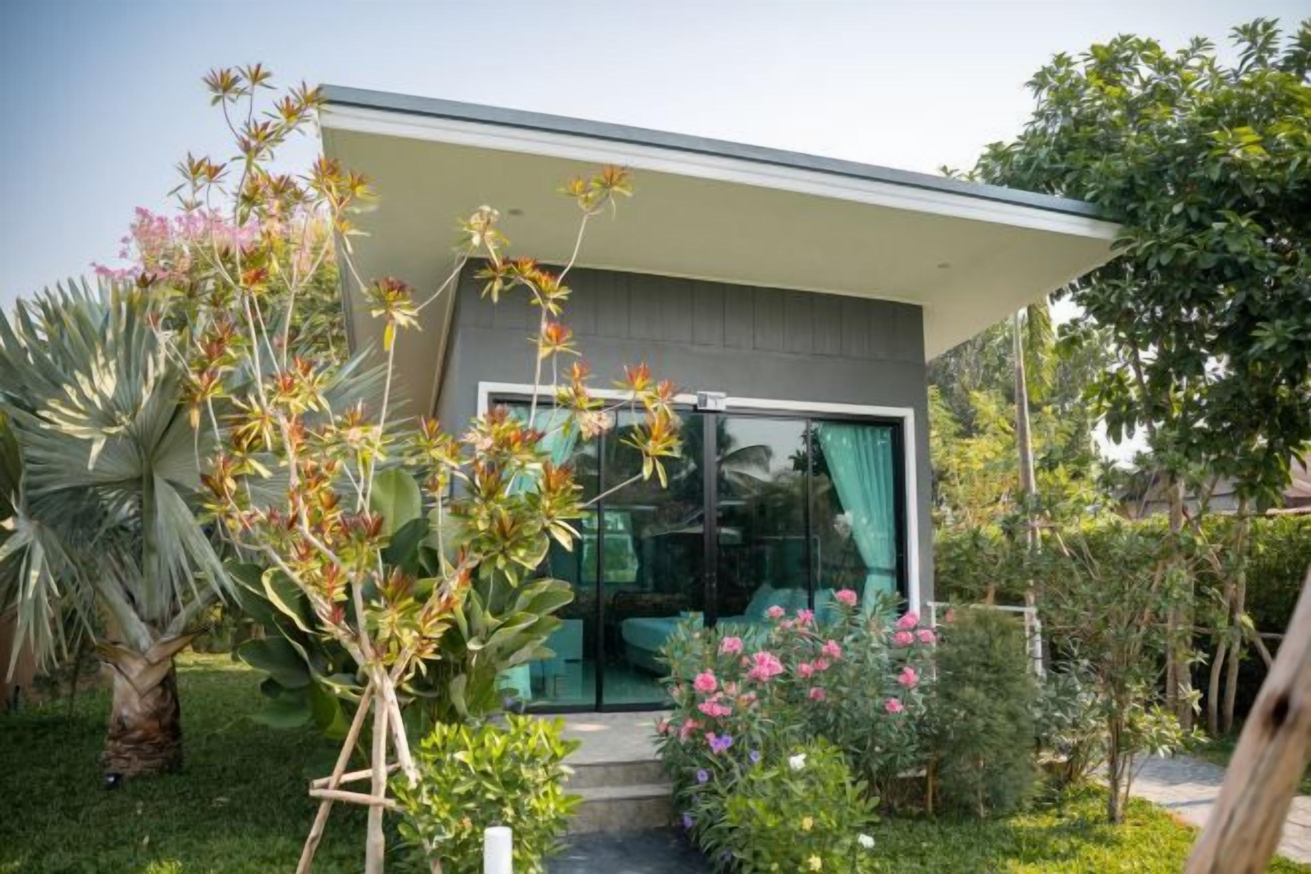 Una casa moderna con puerta de vidrio, rodeada por un jardín con diversas plantas y flores.