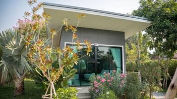 Una casa moderna con puerta de vidrio, rodeada por un jardín con diversas plantas y flores.