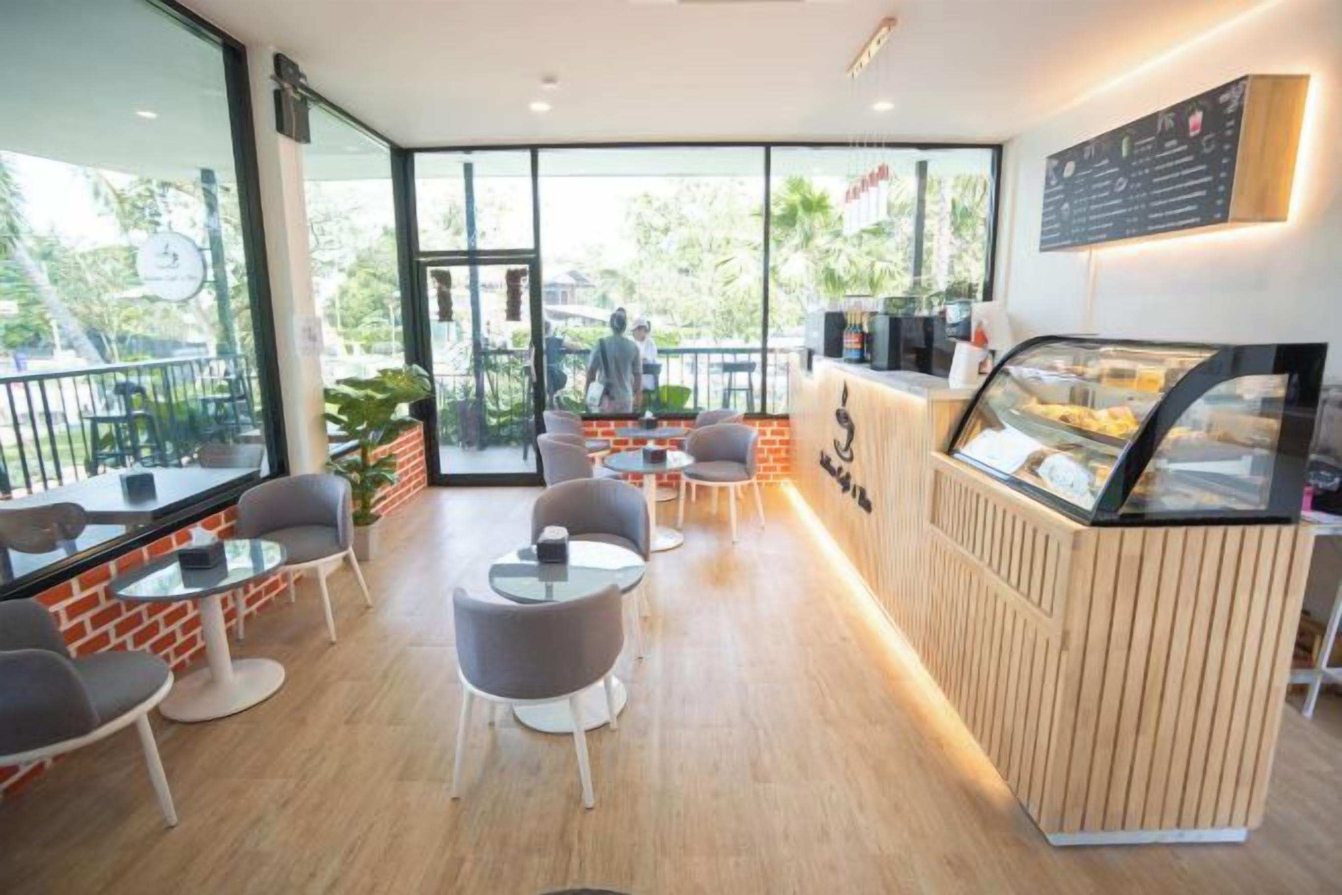 Ein Café mit Holztresen, einer Glastheke und einem Sitzbereich mit Tischen und Stühlen.