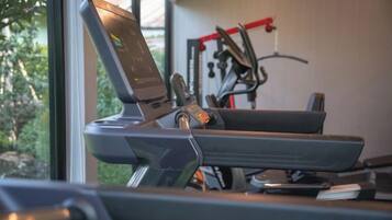 A treadmill with a digital display, a window with a view of greenery, and exercise equipment in the background.