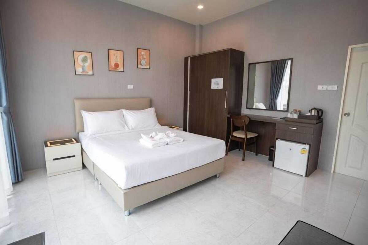 Ein Hotelzimmer mit Bett, Schreibtisch, Stuhl, Kleiderschrank und kleiner Kommode.