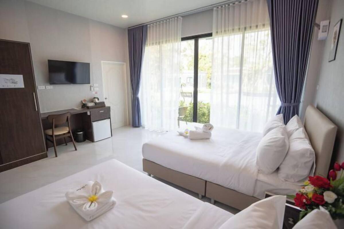 Ein Hotelzimmer mit zwei Betten, einem Schreibtisch, einem Fernseher und einem Fenster mit Vorhängen.