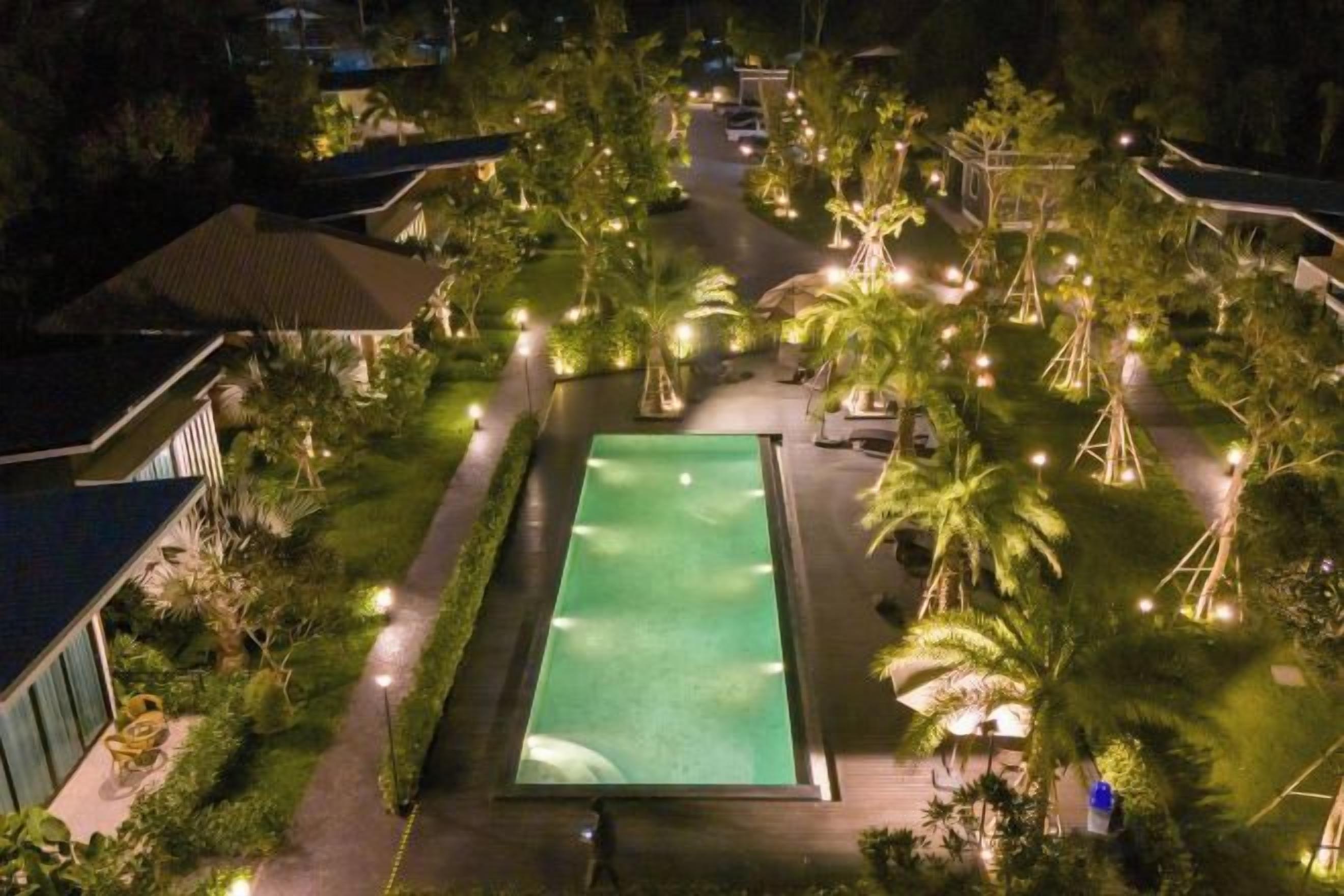 A pool surrounded by palm trees and pathways, with buildings in the background.