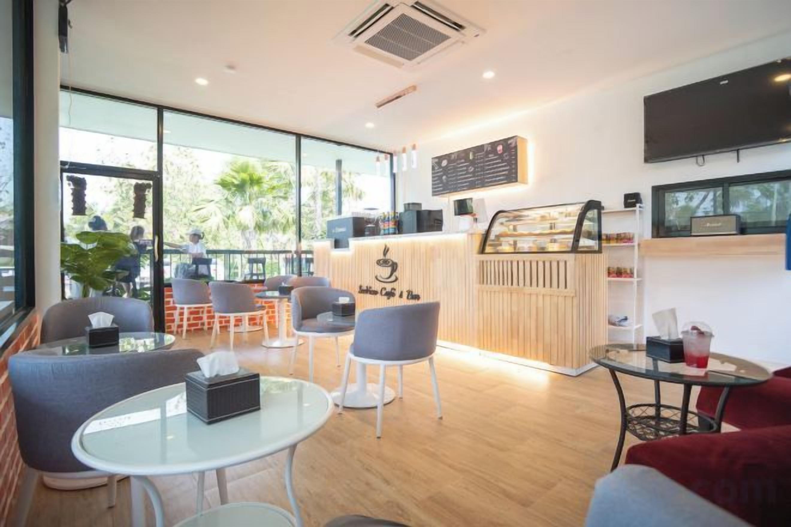 A modern cafe with a wooden counter, seating area with tables and chairs, and large windows offering a view of the outdoors.