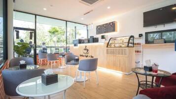 A modern cafe with a wooden counter, seating area with tables and chairs, and large windows offering a view of the outdoors.