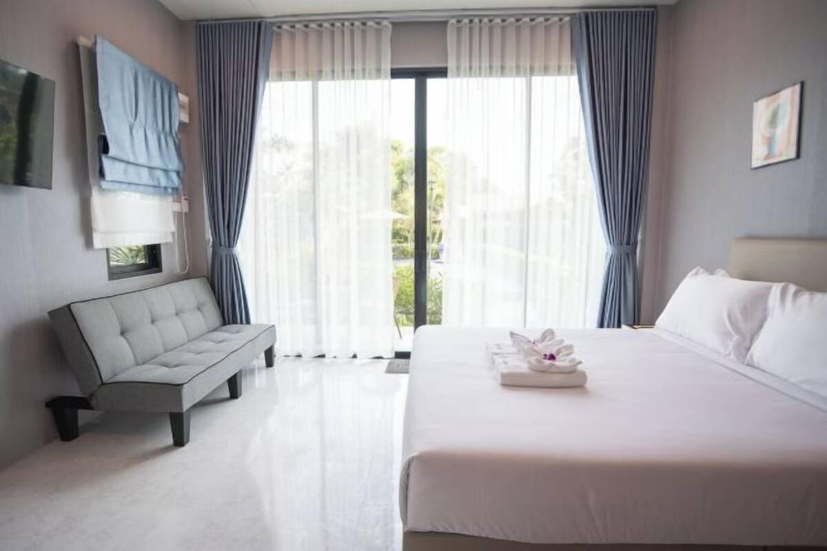 Ein modernes Hotelzimmer mit einem großen Bett, einer Couch, einem Flachbildfernseher und Blick auf Grün durch die Fenster.