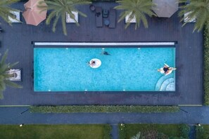 An aerial view of a rectangular swimming pool with two people and a floating device, surrounded by palm trees and outdoor seating. - Seeview Resort (Phetchabun)
