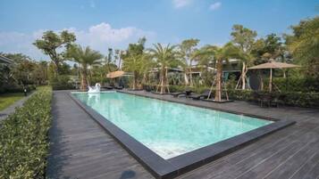 A rectangular swimming pool with a dark wooden deck, surrounded by palm trees and lounge chairs.