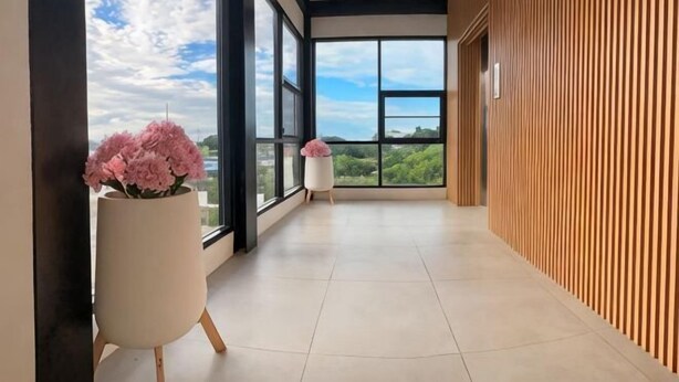 En moderne hotelgang med store vinduer, trævæg og en potteplante med lyserøde blomster.