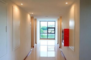 A corridor with a glass door leading to a balcony, white walls, and a red object on the right. - The D257 Hotel (Phetchabun)