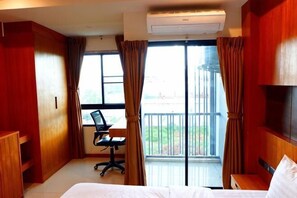 Une chambre d’hôtel comprenant un lit, un bureau, un fauteuil de bureau, une fenêtre avec des rideaux et un balcon.