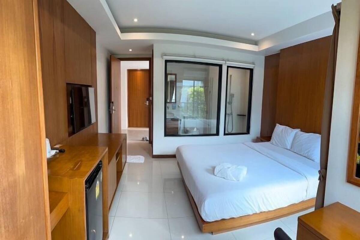 A modern hotel room with a large bed, a wooden desk, a flat-screen TV, and a sliding glass door to the balcony.