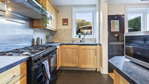 Een moderne keuken met een gasfornuis, oven, houten kasten en een inbouwkoelkast.