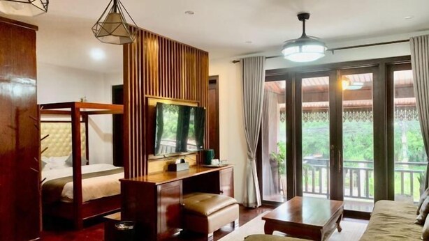 A hotel room with a bed, a desk with a television, a sofa, and a balcony with curtains. - Happy Hour Boutique​ Hotel (Luang Prabang)