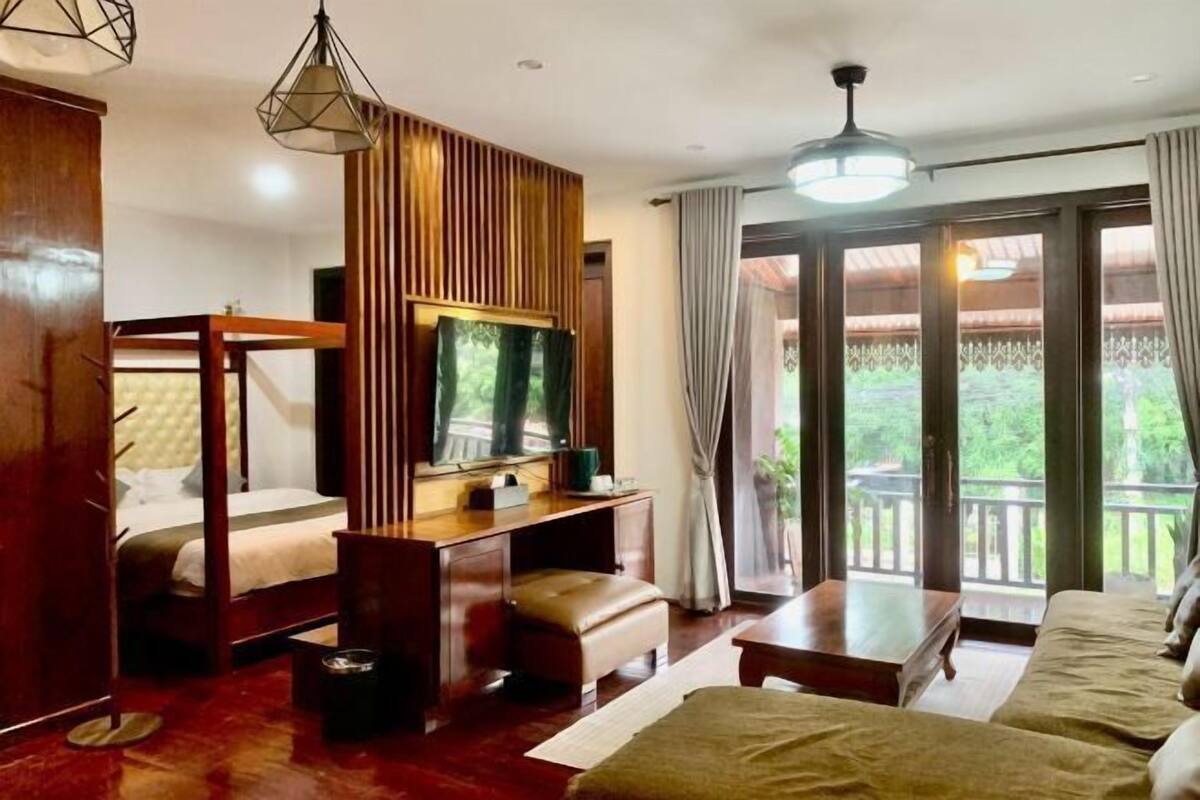 A hotel room with a bed, a desk with a television, a sofa, and a balcony with curtains.