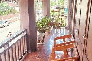 A balcony with wooden chairs, a potted plant, and a view of the street. - Happy Hour Boutique​ Hotel (Luang Prabang)