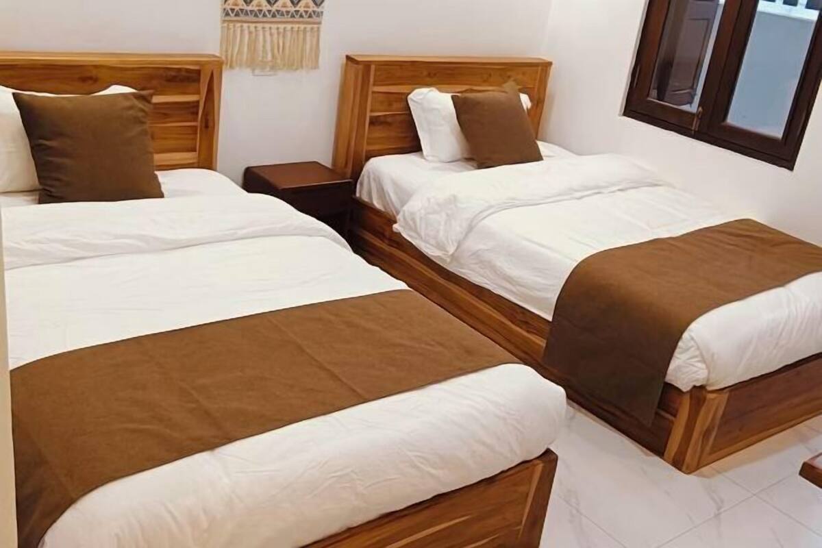 A hotel room with two wooden beds, white bedding, and a brown throw blanket.