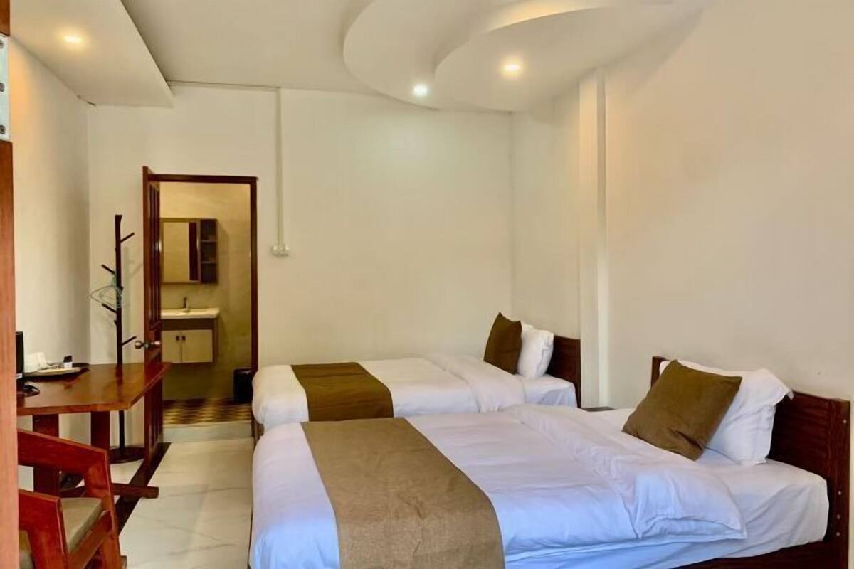 A hotel room with two beds, a wooden desk, and a bathroom visible through an open door.