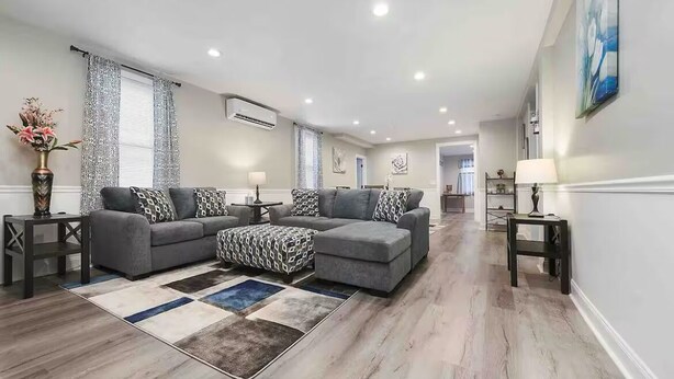 Ein geräumiges Wohnzimmer mit einem grauen Ecksofa, gemusterten Zierkissen und einem farbenfrohen Teppich.