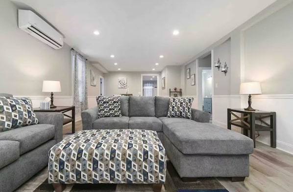 A modern living room with a grey sectional sofa, a matching ottoman, and two side tables with lamps.