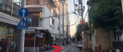 A street with a pedestrian crossing, a directional sign, and a building with a storefront.