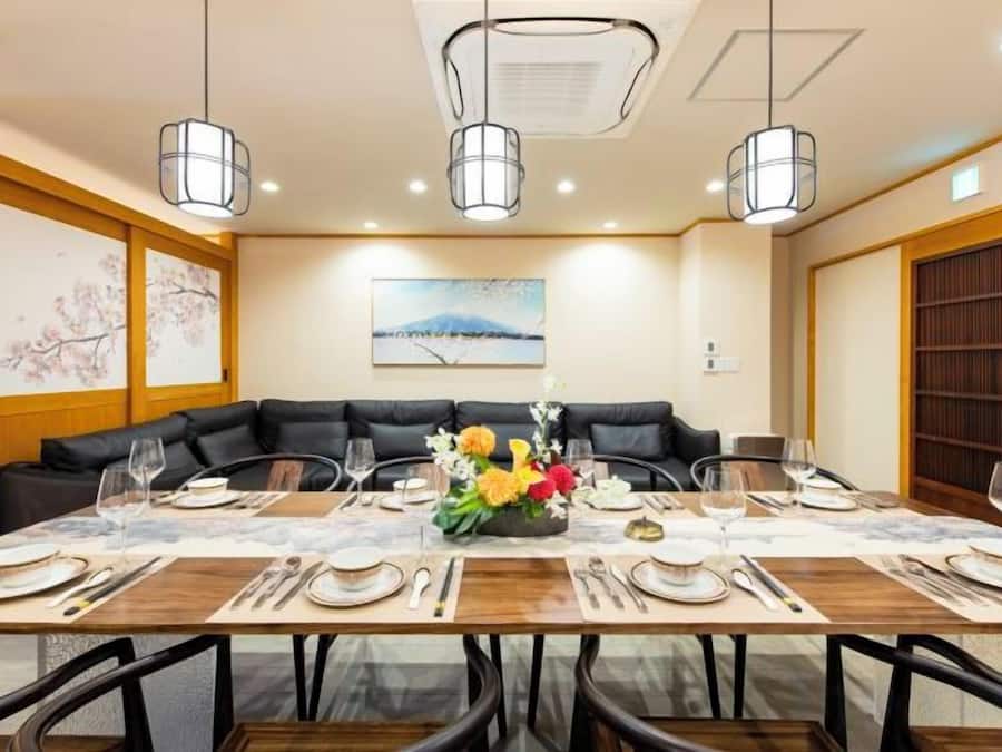 A dining area with a long table, black leather sofa, and hanging pendant lights.