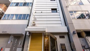 A multi-story building with a modern facade, a ground-level entrance with a yellow door, and a visible air conditioning unit.
