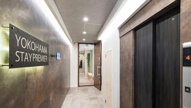 Un couloir avec une pancarte indiquant « YOKOHAMA STAY PREMIER », un ascenseur et une porte donnant sur une autre pièce.