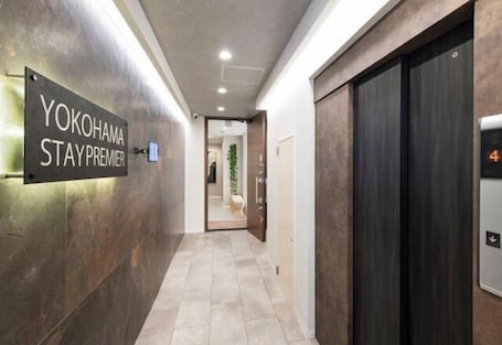 A hallway with a sign reading 'YOKOHAMA STAY PREMIER,' an elevator, and a door leading to another room.