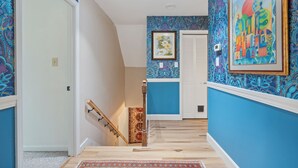 Un pasillo con paredes azules, una escalera de madera y una alfombra estampada.
