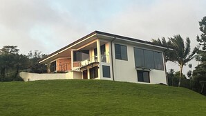 Une maison moderne dotée d’un grand balcon, située sur une colline verdoyante.