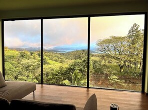 A room with a large window offering a view of a lush landscape with trees and hills. - Welcoming 3-bedroom house with WiFi in Nuevo Arenal (Tilaran)