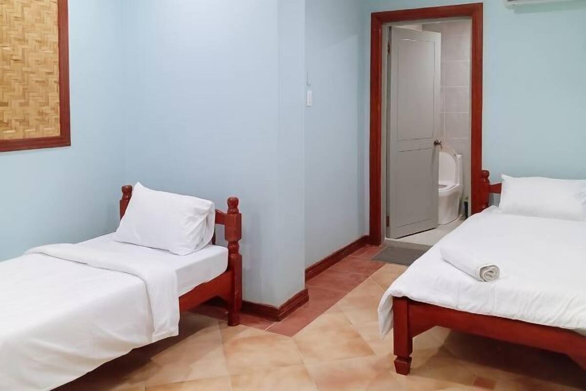 A room with two single beds, a wooden door, and a tiled floor.