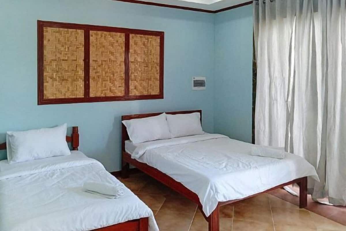 A room with two beds, a woven headboard, a curtain, and a tiled floor.