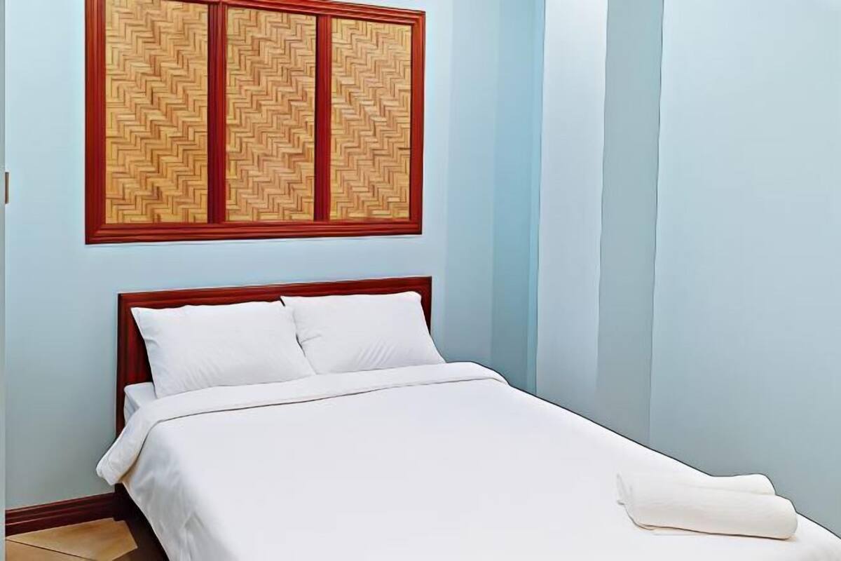 A bed with white bedding, a wooden headboard, and a wall with a patterned panel.