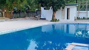 A swimming pool with clear blue water, surrounded by a tiled deck and a small white building with a door. - McKinley Grand Marina Hotel and Resort (Guihulngan)