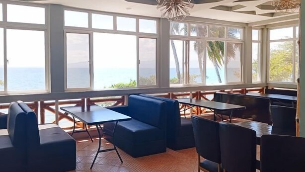 A restaurant with large windows, black seating, and a view of the sea. - McKinley Grand Marina Hotel and Resort (Guihulngan)