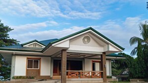 A two-story house with a green roof, a covered porch with wooden railings, and a small garden area. - McKinley Grand Marina Hotel and Resort (Guihulngan)
