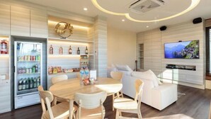 A modern living room with a wooden dining table, white sofas, and a flat-screen TV mounted on the wall. - Jaidee Pool Villa (Hat Yai)
