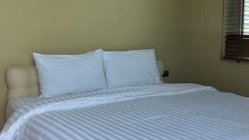 Una cama con una colcha a rayas y dos almohadas en una habitación con una pared lisa y un ventanal con persianas.