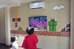A room with a television displaying a video game, a wall-mounted air conditioner, and a wall with a Mario-themed design. - Jaidee Pool Villa (Hat Yai)